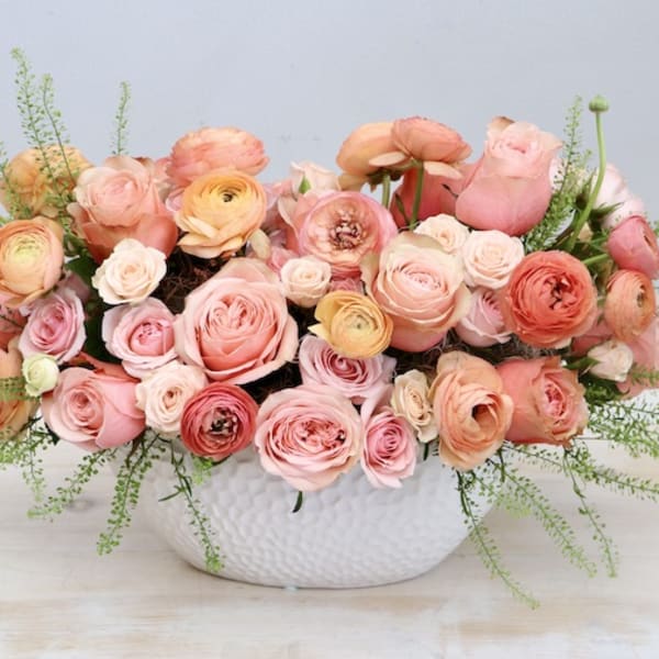 Low centerpiece of peach and pink roses and ranunculus in a white ceramic bowl