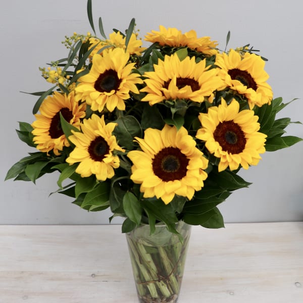 Tall glass vase of bright yellow sunflowers with dark centers arranged in a full bouquet