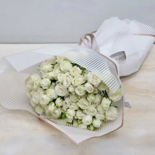 Large bouquet of white roses wrapped in striped white paper with a ribbon.