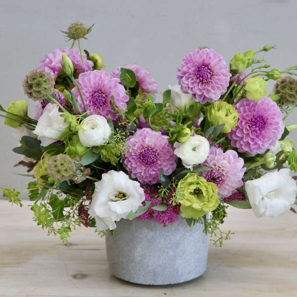Low arrangement of pink dahlias with white and green blooms in a gray pot.