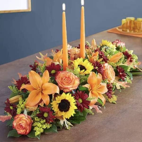 Long floral centerpiece with two orange taper candles