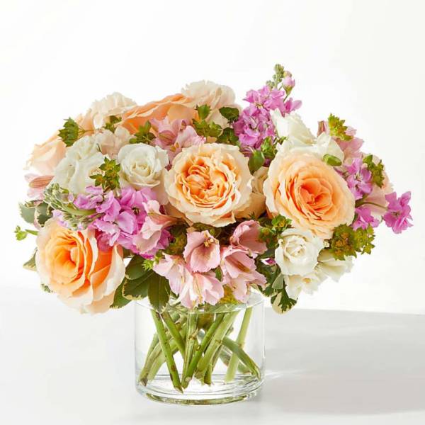 Peach and white roses with pink flowers in a clear glass vase