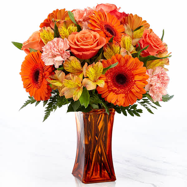 Orange and pink mixed bouquet in an amber glass vase