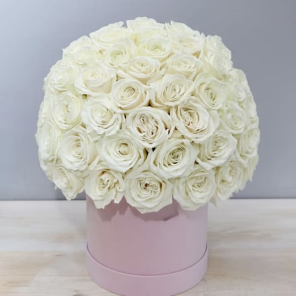 Round arrangement of ivory roses tightly packed in a pale pink hat box on a light table