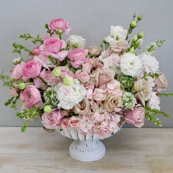 Low compote arrangement of pink and blush roses, hydrangeas, and white lisianthus in a white pedestal bowl