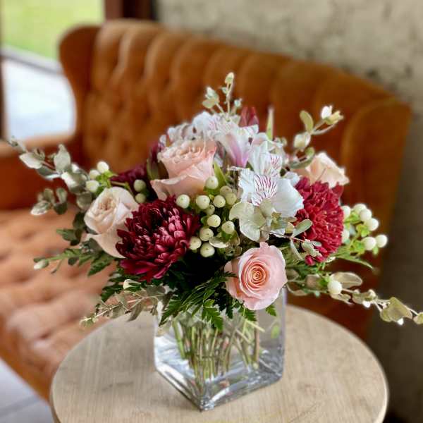 Pink and burgundy flowers arranged in a clear square vase