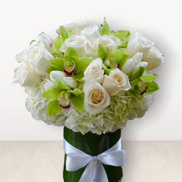 White roses and green orchids in a tall vase with a white ribbon