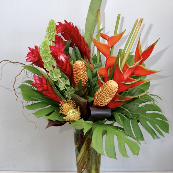 Tropical bouquet with red and orange flowers in a tall glass vase