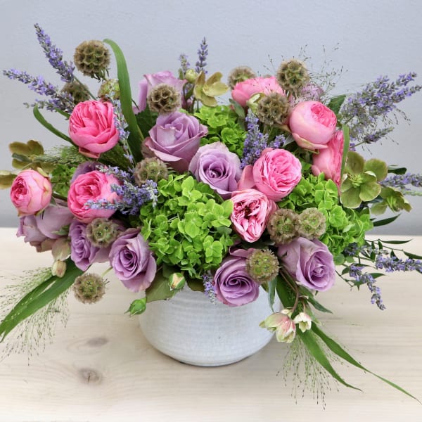 Low arrangement of pink and lavender roses with green hydrangeas in a white bowl vase