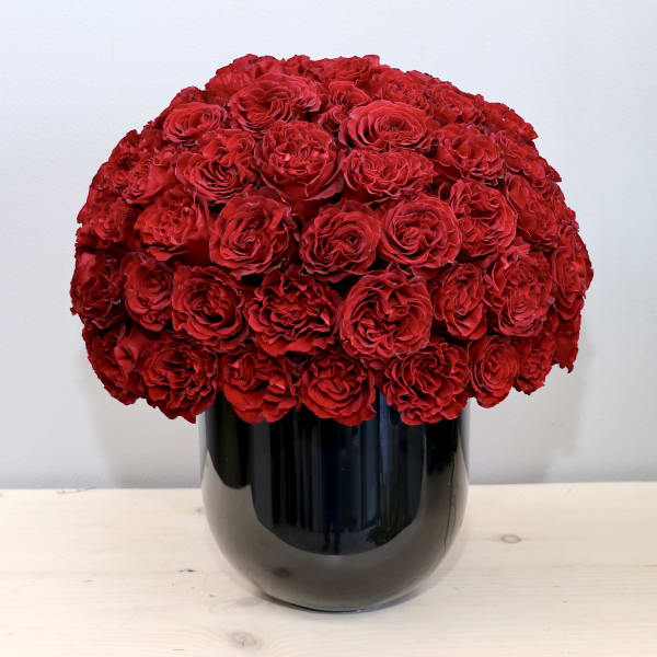 Dense dome of red roses arranged tightly in a glossy black cylindrical vase