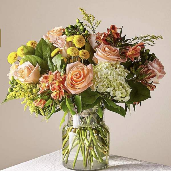 Bouquet of peach roses, yellow blooms, and white hydrangea in a glass vase