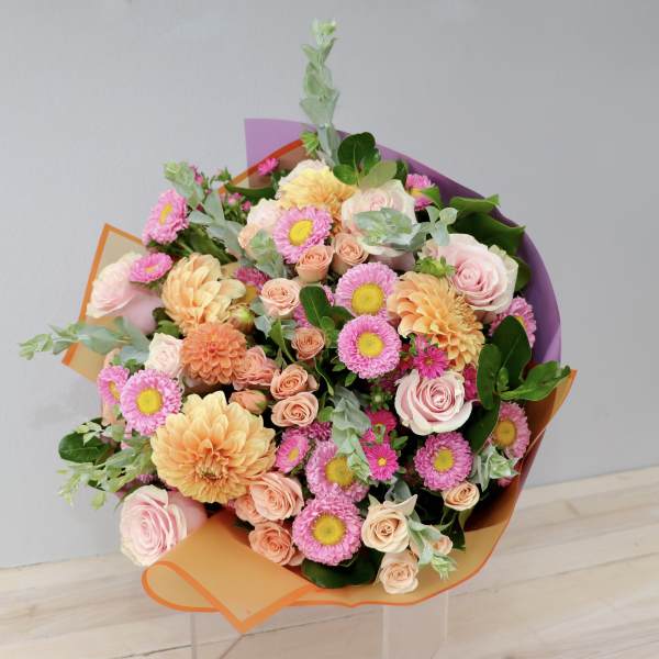 Bouquet of pink and peach flowers wrapped in orange and purple paper