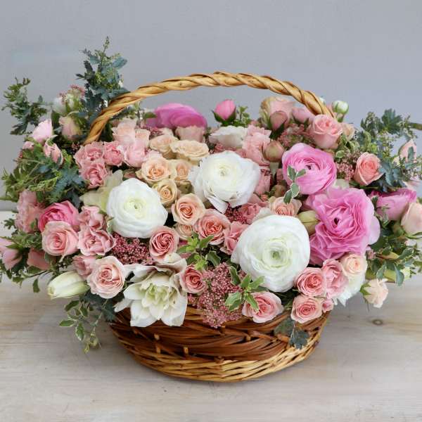 Low basket arrangement of pink and white roses and ranunculus in a woven wicker basket