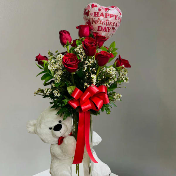 Red roses in a vase with a heart-shaped Valentine balloon and teddy bear