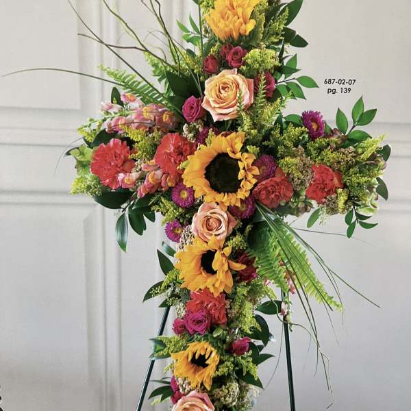 Large floral cross with sunflowers, roses, and carnations on a stand