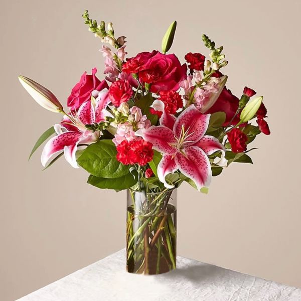 Bouquet of pink lilies, red roses, and carnations in a clear glass vase