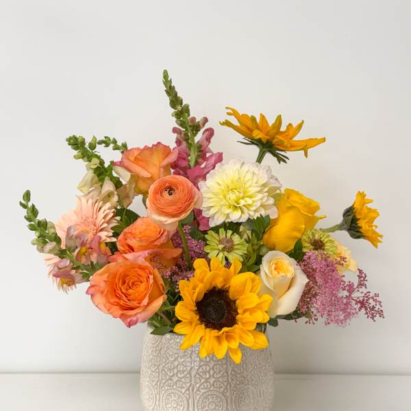 Mixed bouquet of orange, yellow, pink, and white flowers in a patterned vase