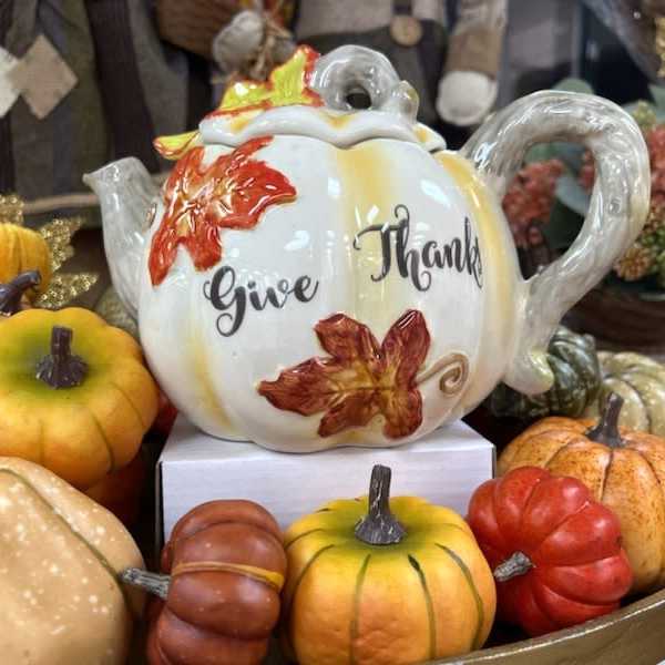 Decorative ceramic teapot surrounded by assorted pumpkins and gourds