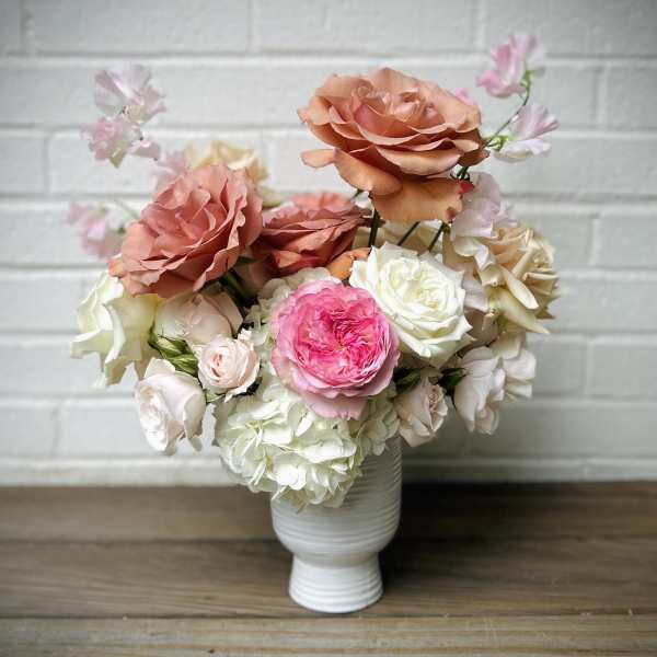 Peach, pink, and white roses arranged in a white vase
