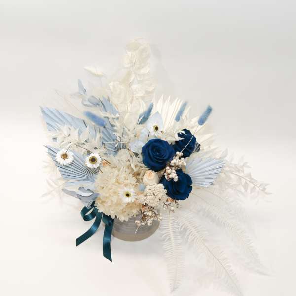 Blue and white floral arrangement in a round container with ribbon