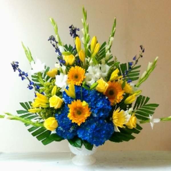 Tall blue, yellow, and white flower arrangement in a white pedestal vase.