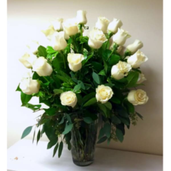 White roses arranged in a clear glass vase with lush greenery