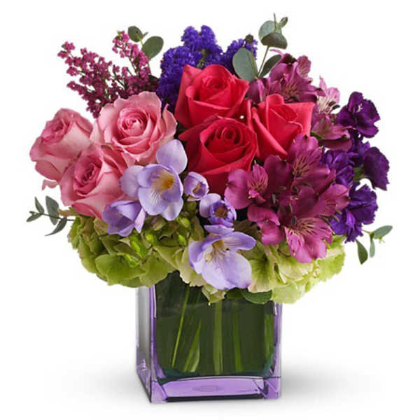 Mixed bouquet of pink, red, purple, and lavender flowers in a square glass vase