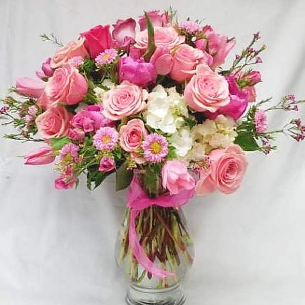 Pink roses and small white flowers in a glass vase with a pink ribbon