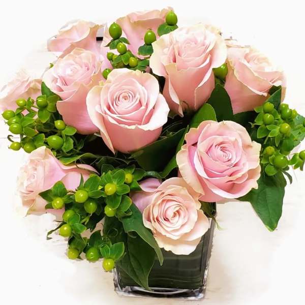 Pink roses arranged in a clear square vase with green berries