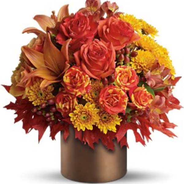 Autumn arrangement of orange roses, lilies, and yellow mums in a bronze cylinder vase