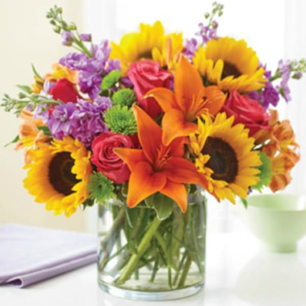 Bouquet of sunflowers, orange lilies, red roses, and purple flowers in a glass vase