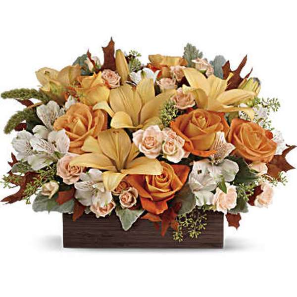 Low centerpiece of orange roses, yellow lilies, and white blooms in a dark rectangular container