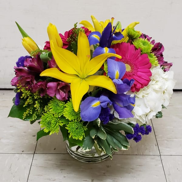 Bright mixed bouquet with yellow lilies, purple irises, pink gerberas, and white hydrangeas in a glass vase