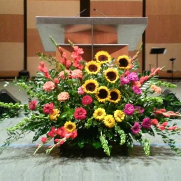 Large stage arrangement of yellow sunflowers with pink and orange flowers in front of a podium