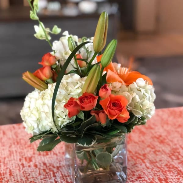 Orange roses and white hydrangeas in a square glass vase
