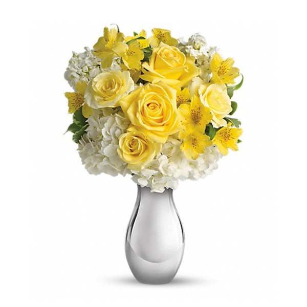 Yellow roses and white flowers arranged in a clear glass vase