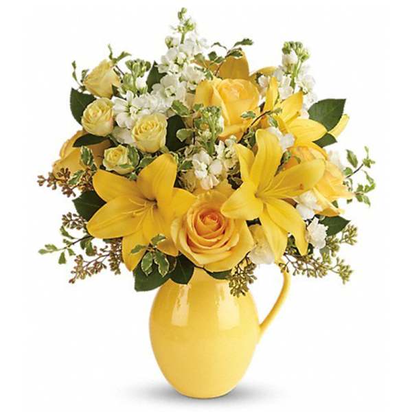 Yellow lilies and roses arranged in a yellow pitcher vase