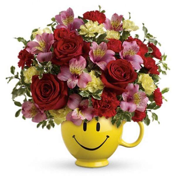 Bouquet of red roses and pink flowers in a yellow smiley-face mug