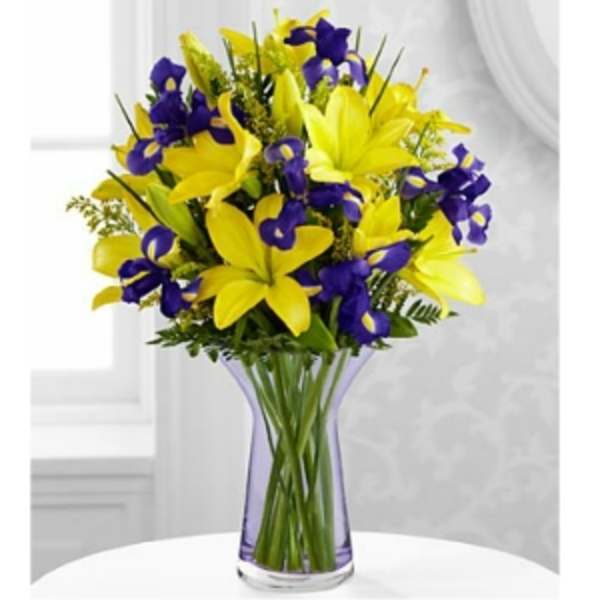 Yellow lilies and purple irises in a clear vase