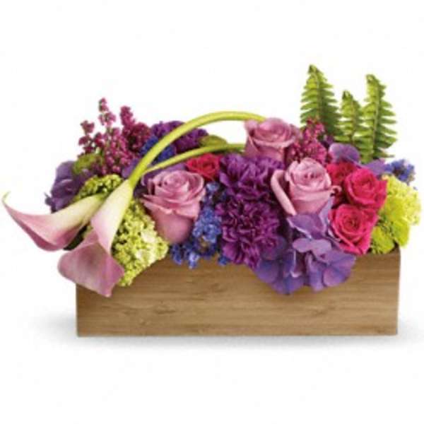 Low rectangular arrangement of pink and purple flowers with calla lilies and ferns in a wooden box.