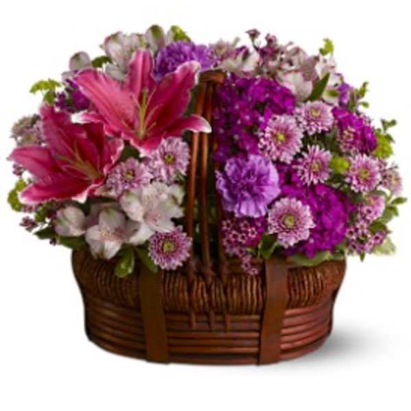 Low basket arrangement of pink lilies, purple mums, carnations, and white alstroemeria in a brown wicker basket