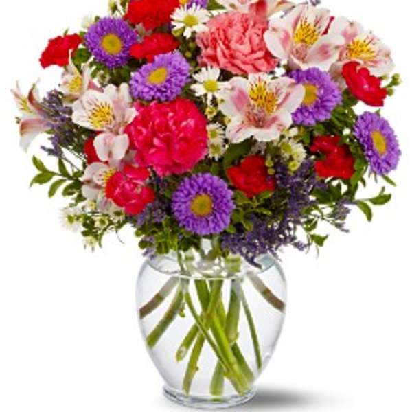 Mixed bouquet of pink, purple, and red flowers in a clear glass vase