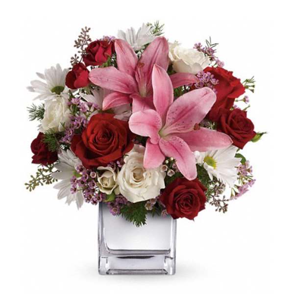 Bouquet of pink lilies, red and white roses, and white daisies in a clear glass vase