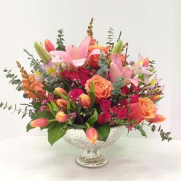 Mixed pink, orange, and yellow flowers in a clear pedestal bowl