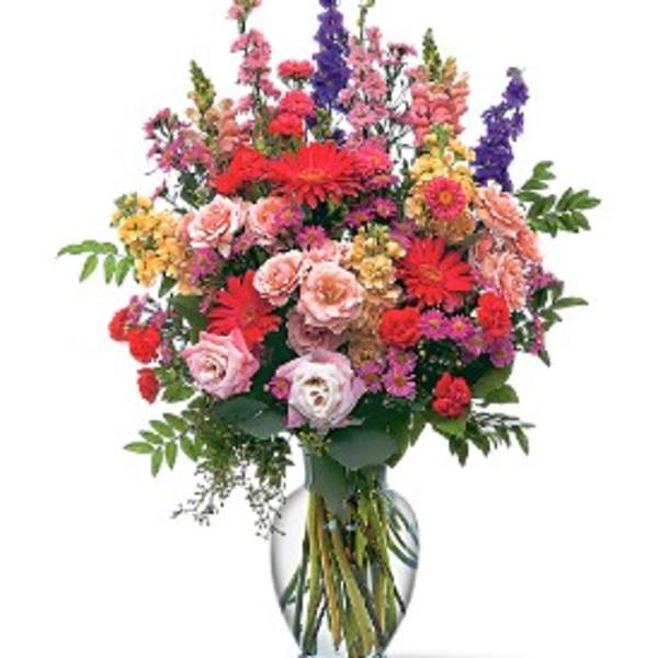 Tall mixed bouquet of pink, red, purple, and yellow flowers in a glass vase
