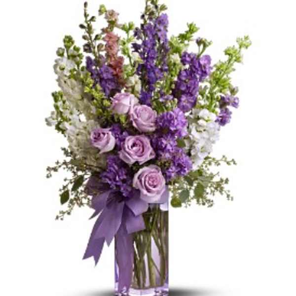 Lavender roses and purple stock in a clear square vase with a purple ribbon