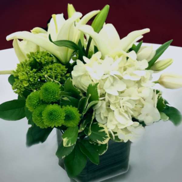 White lilies and hydrangeas with green pompons in a dark vase
