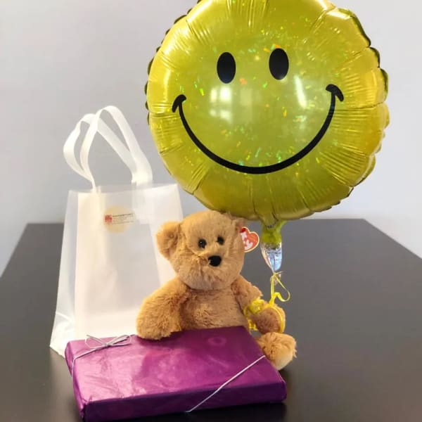 Teddy bear with a smiley balloon, gift bag, and wrapped box
