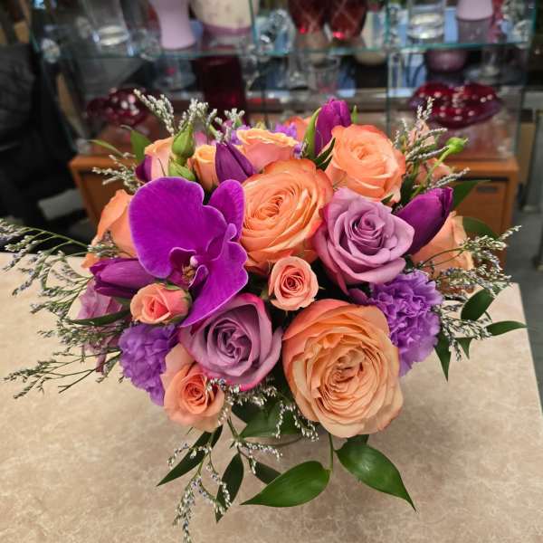 Bouquet of peach, lavender, and purple roses with orchids in a vase