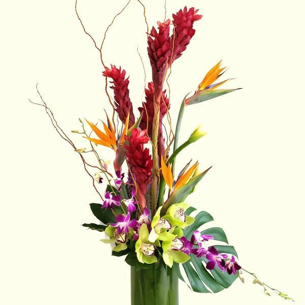Tall tropical arrangement with orchids and bird of paradise in a glass vase